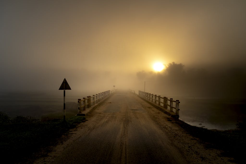 A serene sunrise scene of a foggy bridge enveloped in mist, casting a moody atmosphere.