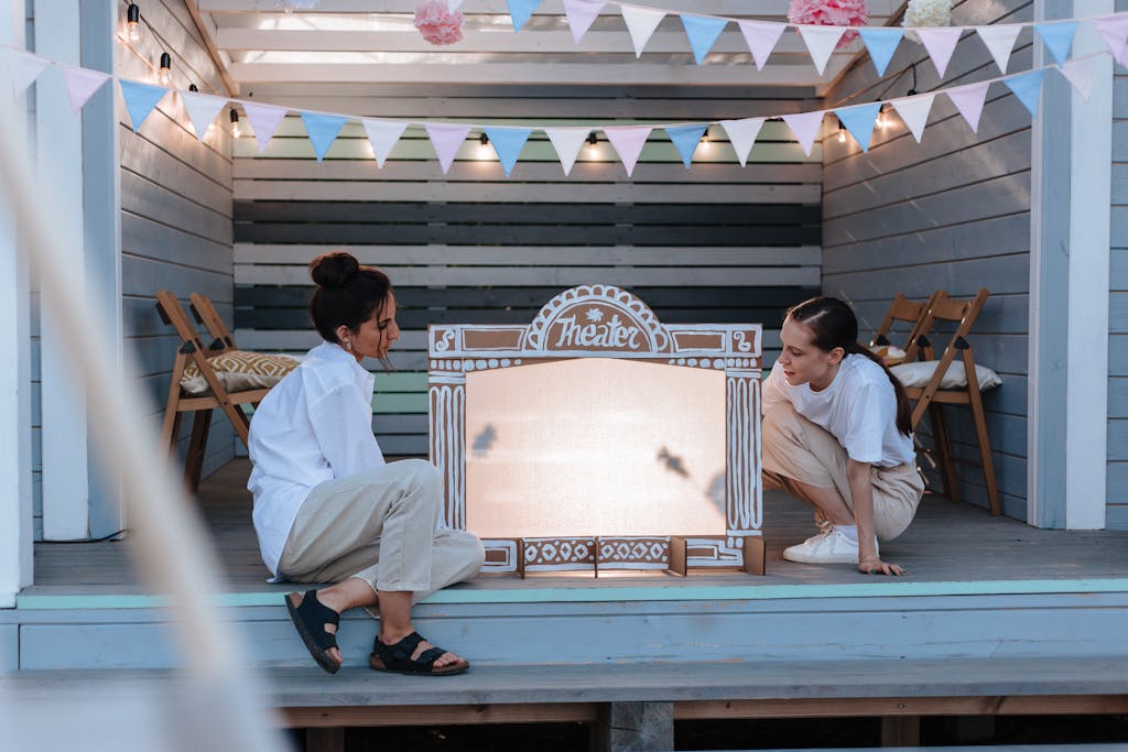 Two women engage in a creative shadow puppet play in an outdoor theater setup.